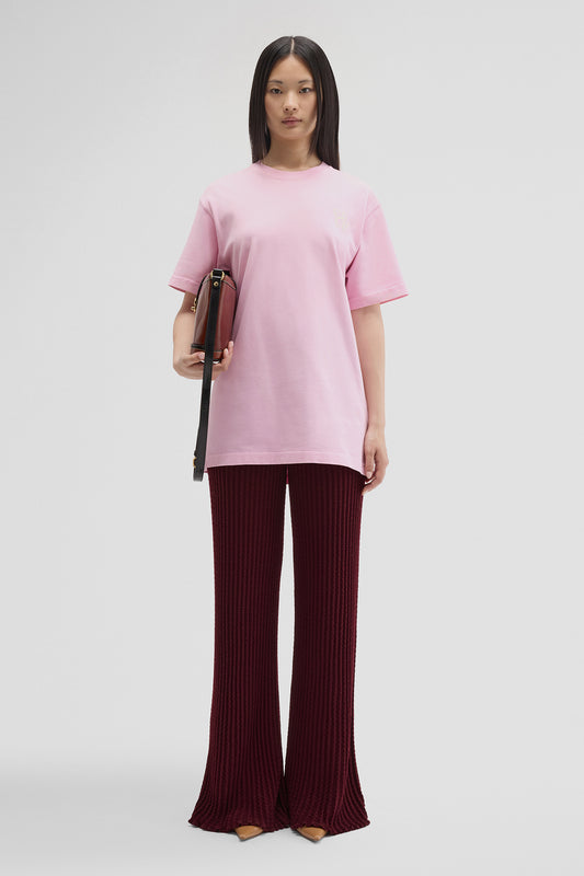 Woman wearing a pink top and burgundy pants holding a brown bag on a white background